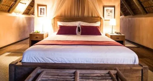 Quarto com cama de casal e almofadas vermelhas debaixo do telhado de colmo