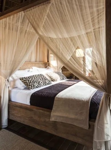 Cama de madeira com dossel de rede mosquiteira num bungalow